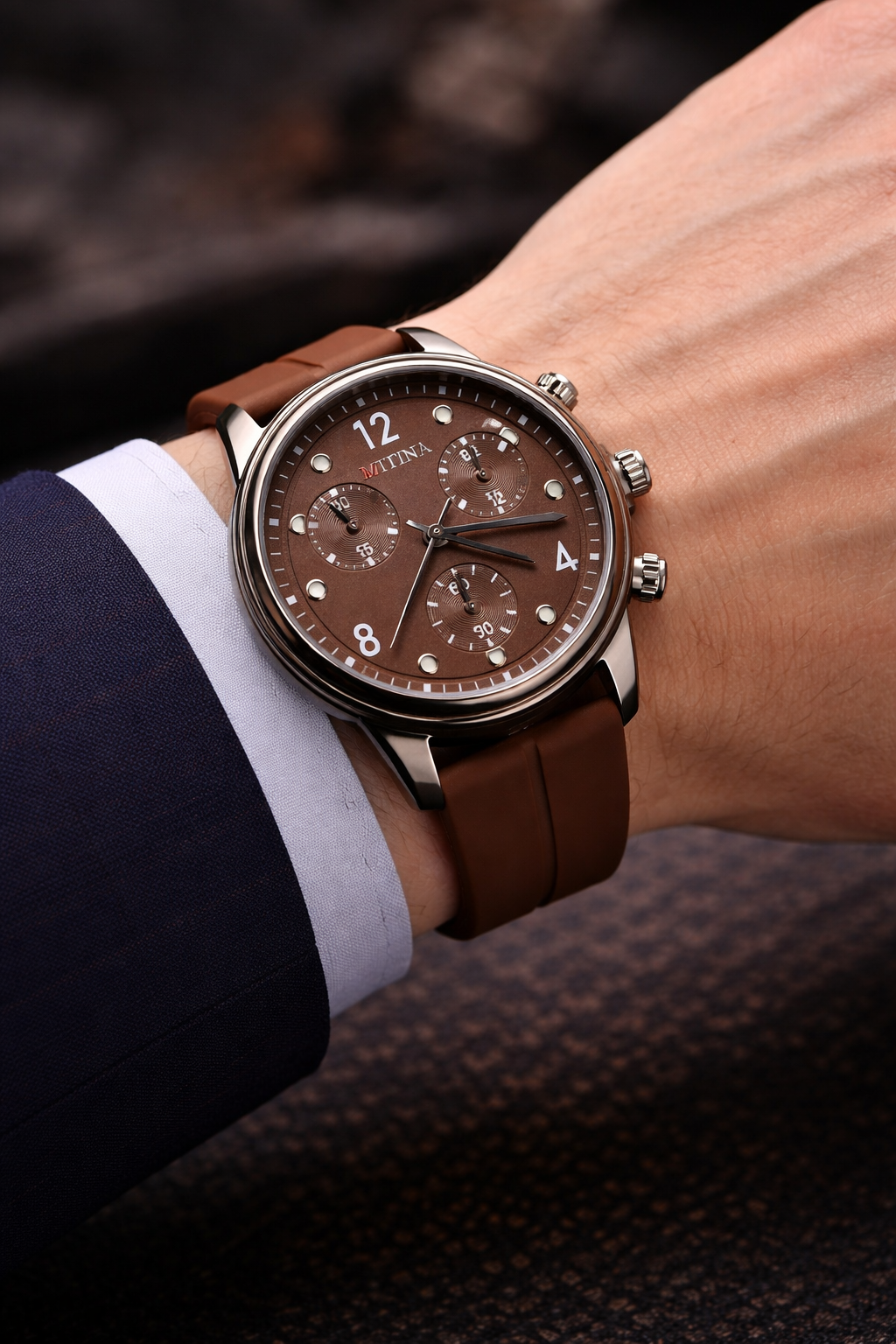 Brown wristwatch with leather strap on a person's wrist, wearing a suit.